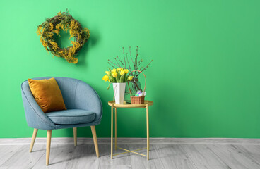 Comfortable armchair, table with tulips and basket of Easter eggs near color wall
