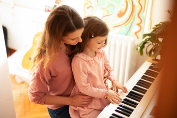 Woman and girl playing a piano. Beautiful mom teaching her daughter playing a piano.