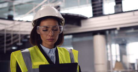 Close up of female architect standing inside empty office center holding a tablet checking building plan. Beautiful woman senior engineer controlling costruction process.