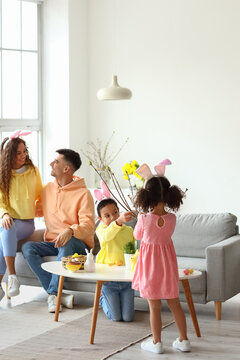 Little children with their parents decorating tree branches at home on Easter day