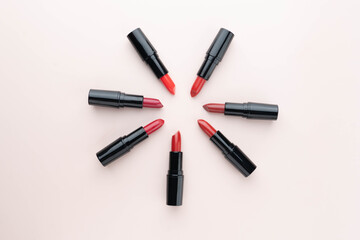 Red lipsticks of different shades arranged in a circle on beige background. Makeup and cosmetics concept. Flat layout.