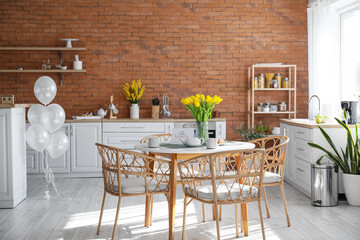 Teapot, cups, tulips and greeting card on dining table in kitchen interior. International Women's Day celebration