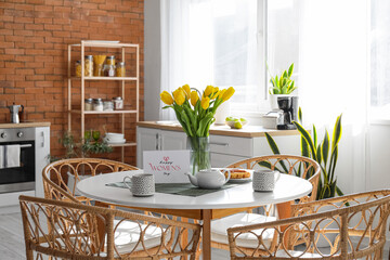 Teapot, cups, tulips and greeting card with text HAPPY WOMEN'S DAY on dining table in stylish kitchen