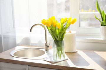 Vase with beautiful tulips near sink on kitchen counter
