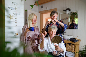 Happy senior women friends in bathrobes having fun indoors in bathroom, selfcare concept.