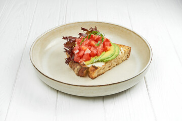 Bruschetta with tomatoes, salmon and avocado in a plate on a white wooden background
