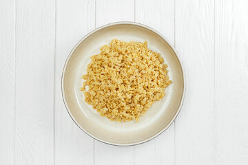 Dietary bulgur in a plate on a white wooden background