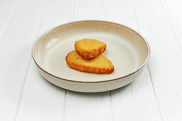 Chicken cutlet in breading on a plate on a white wooden background