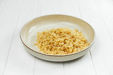 Dietary bulgur in a plate on a white wooden background