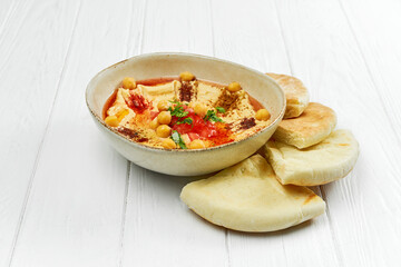Hummus with tomatoes and chickpeas, pita bread on a white wooden plate