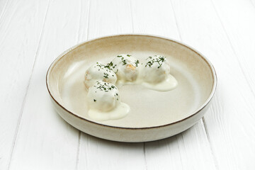 Chicken meatballs with white sauce in a plate on a white wooden background