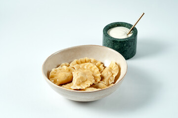 Dumplings with different fillings in a bowl with sour cream on a white background. Varenyky
