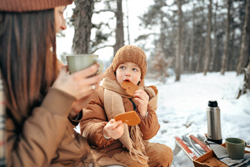 Young woman with a son in winter forest on a picnic drink hot tea