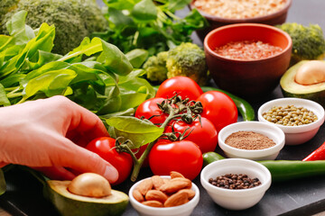 Fresh vegetable close up. Woman chef hand holding fruit, taking tomato, green leaves, arugula, avocado fruit, chilly peppers, broccoli, almond, spices. Vegan food, vegetarian diet