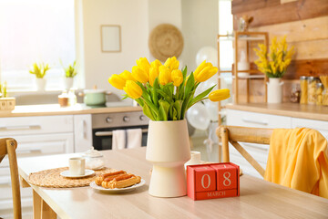 Cube calendar with date 8 MARCH, tulips, dessert and cup on dining table. International Women's Day celebration