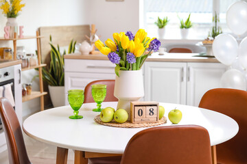 Vase with beautiful flowers, fresh apples, glasses and cube calendar on dining table. International Women's Day celebration