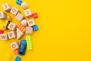 Wooden cubes, plastic constructor and cars toy on bright yellow background, concept flat lay about...