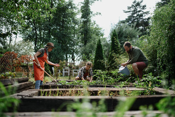 Happy young and old farmers working with garden tools outdoors at community farm.