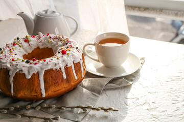 Tasty Easter cake with cup of tea and pussy willow branches on light table