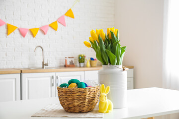 Wicker basket with Easter eggs, rabbit and bouquet of tulips on dining table in kitchen
