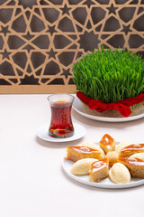 Green fresh semeni sabzi wheat grass in white plate with traditional Azerbaijani pastry shekerbura and pakhlava with wooden shebeke pattern, Novruz spring equinox celebration in Azerbaijan