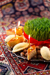 Beautiful Novruz tray on rug with semeni - wheat grass, pakhlava, shekerbura and festive candles on national Azerbaijani carpet table cloth. Spring equinox and new year celebration in Baku.