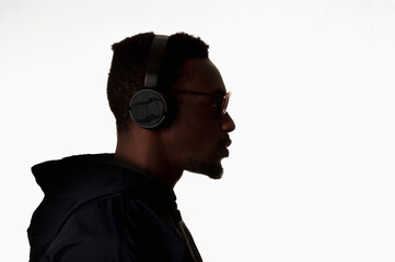 Black man with headphones on white background. Person listening to music with sunglasses. Side view