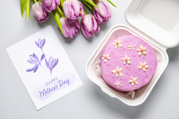 Plastic lunch box with tasty bento cake, greeting card and flowers on grey background