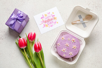 Plastic lunch box with tasty bento cake, greeting card and flowers on light background