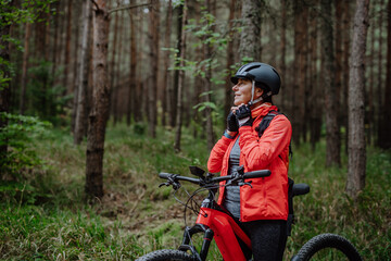 Plakat Senior woman biker putting on cycling helmet outdoors in forest in autumn day.