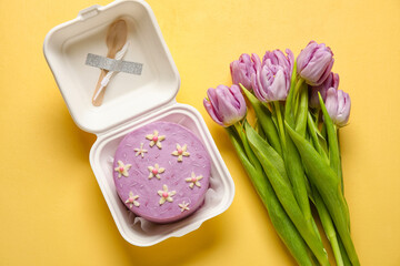 Plastic lunch box with tasty bento cake and flowers on orange background