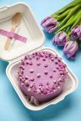 Plastic lunch box with tasty bento cake and flowers on blue background