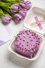 Plastic lunch box with tasty bento cake, envelope and flowers on light background