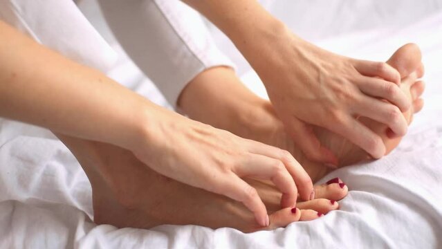 Side view of female hands scratch legs sitting on white bed at home. Itchy skin, fungus, fungal bacterial infection, allergic reaction, eczema, dermatitis of the foot. Health and skincare concept.