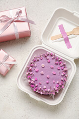 Plastic lunch box with tasty bento cake and gifts on light background