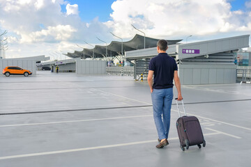 A young man with a suitcase walks in the parking lot outdoors. © Andrii