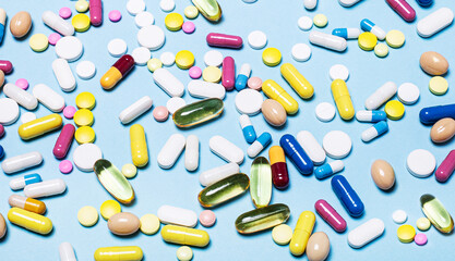 Variety of drugs in capsules and tablets in different colors on a blue background. Medical concept. Pharmaceuticals