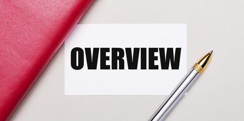On a light gray background, there is a golden pen, a burgundy notebook and a white blank card with a place to insert text OVERVIEW Business concept.