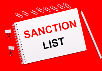 On a bright red background, a white pencil, white paper clips, and a white notebook with the text SANCTION LIST