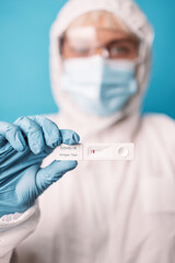 Doctor in blue gloves holding rapid antigen test kit during swab COVID-19 testing over bright blue color background. Pandemic concept
