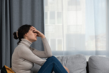 Young sad woman with broken heart sitting alone at home suffering from depression anxiety and bad mental condition. Female having hard time and burnout of overthinking and worry 