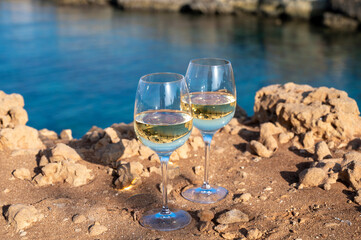 Two glasses of white dry white wine served on rocks in blue sea bay near Protaras touristic town on Cyprus