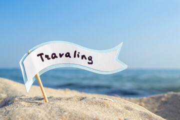 Paper Blue White Blank Speech Bubble on Stick With Word Traveling in Sandy Beach on Background Clean Blue Sky and Sea Close-up on Sunny Summer Day. Concept Travel, Tourism, Vacation, Rest. Copy Space