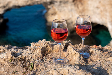Two glasses of rose dry white wine served on rocks in blue sea bay with Love Bridge on background near Ayia Napa touristic town on Cyprus