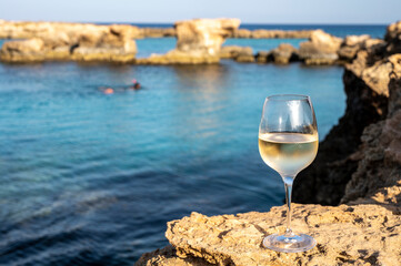 Glass of cold white dry white wine served on rocks in blue sea bay near Protaras touristic town on Cyprus