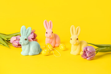 Easter bunnies, eggs and tulip flowers on yellow background
