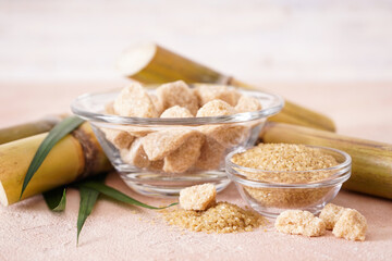 Granulated brown sugar, sugarcane and green leaf on a beige background. Close-up.