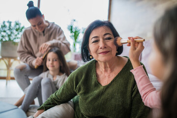 Two happy sisters with mother and grandmother combing hair and doing make up together at home