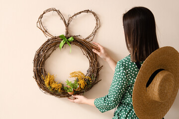 Woman hanging beautiful Easter wreath with mimosa flowers on color wall