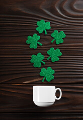 Coffee cup with three leaved shamrock handmade leaves on wooden background